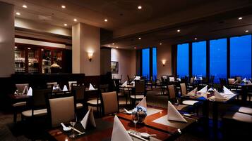 A restaurant with tables set for dining, a bar area, and large windows offering a view.