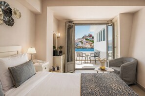 Habitación de hotel con cama, mesita de noche, lámpara, una pequeña mesa con un jarrón y vistas a una piscina y edificios.