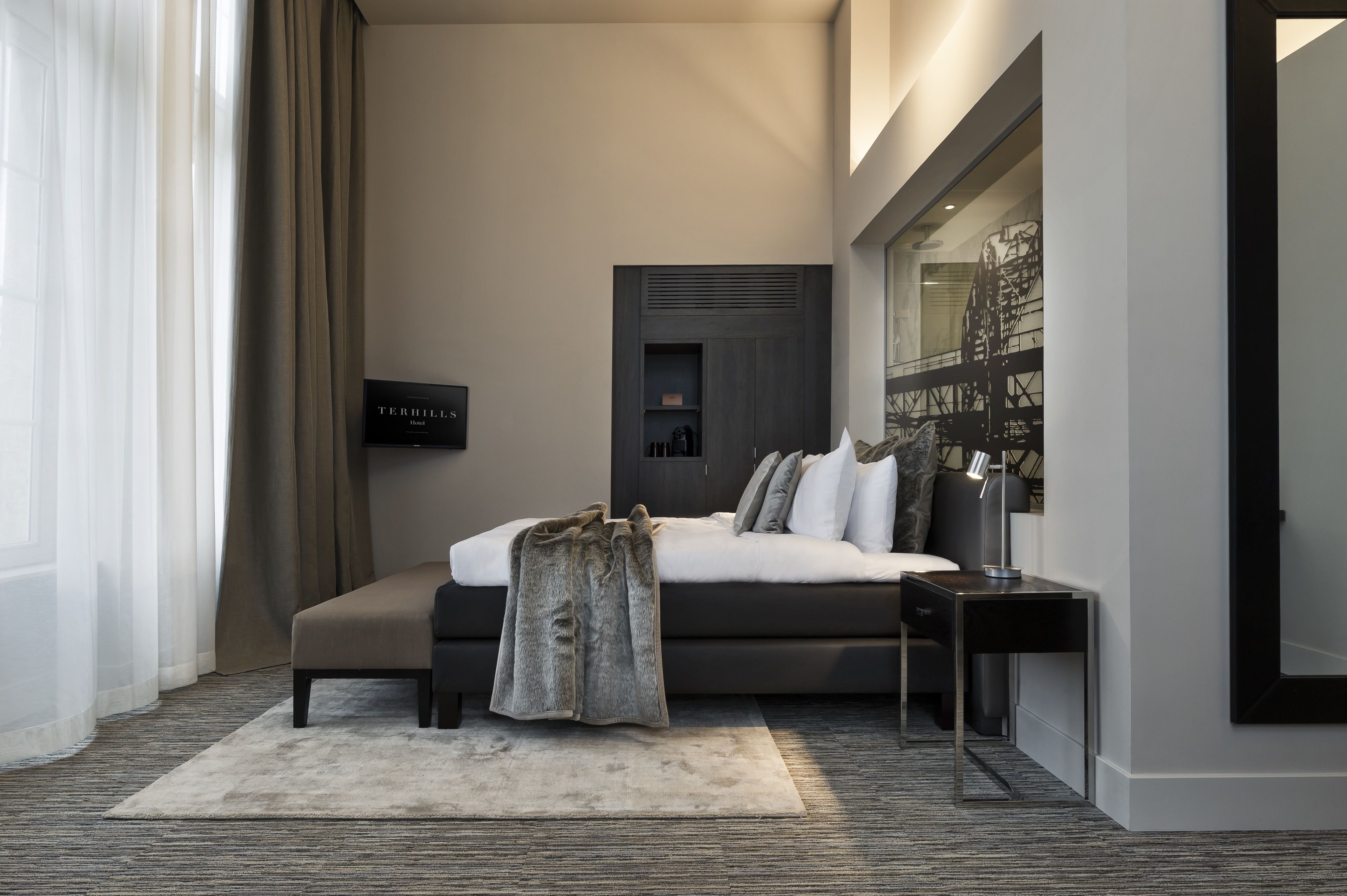 Een moderne hotelkamer met een groot bed, nachtkastje, televisie en een groot raam met gordijnen.