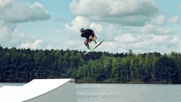 A person performing a jump on a ramp by a lake with a forest in the background.