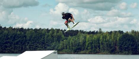 A person performing a jump on a ramp by a lake with a forest in the background.
