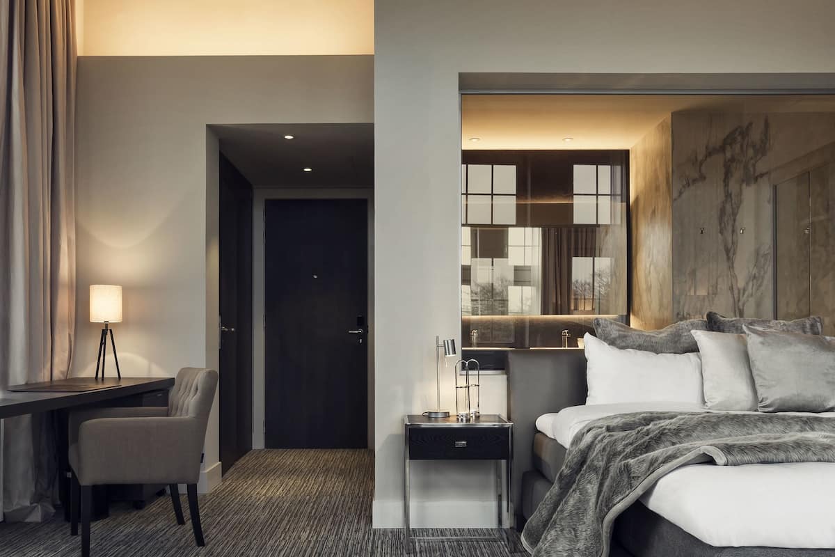 A modern hotel room with a large bed, a desk, and a seating area.