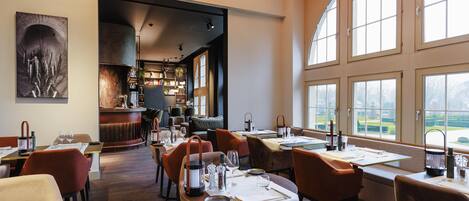 A restaurant with tables set for dining, a bar area, and large windows offering a view.