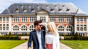 Una pareja caminando frente a un edificio grande y antiguo con fachada simétrica y ventanas de arco.