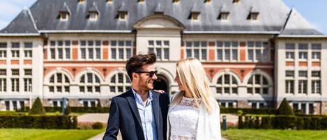 A couple walking in front of a large, historic building with a symmetrical facade and arched windows.
