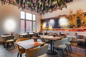 Un interior de restaurante con varias mesas y sillas, un ventanal grande y un mural en la pared.