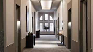 A long, narrow hallway with a carpeted floor, recessed lighting, and a large window at the end.