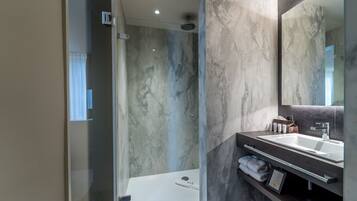 Un baño moderno con ducha de vidrio, pared de mármol, espejo grande y tocador de madera oscura con lavamanos.