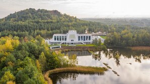 Un edificio moderno con una fachada simétrica, rodeado por un lago y un bosque frondoso.