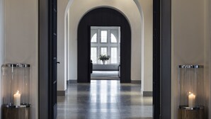 Un pasillo con techo alto, un amplio arco de entrada y vista a una habitación con un gran ventanal.