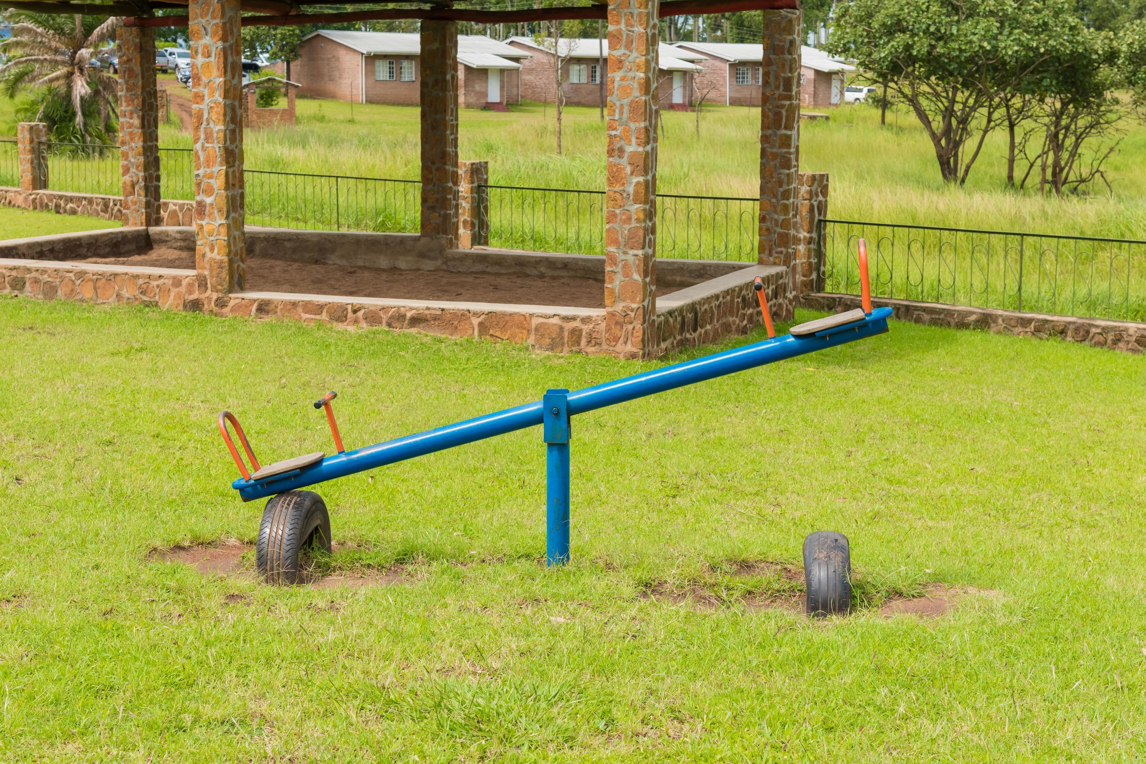 A seesaw in a grassy area with a brick structure in the background.