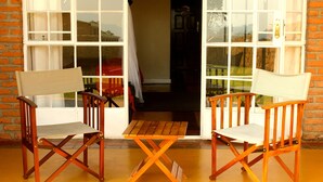 Two wooden chairs and a small table on a yellow floor, with a brick wall and a door leading to a room. - Game Haven Lodge (Chigumula)