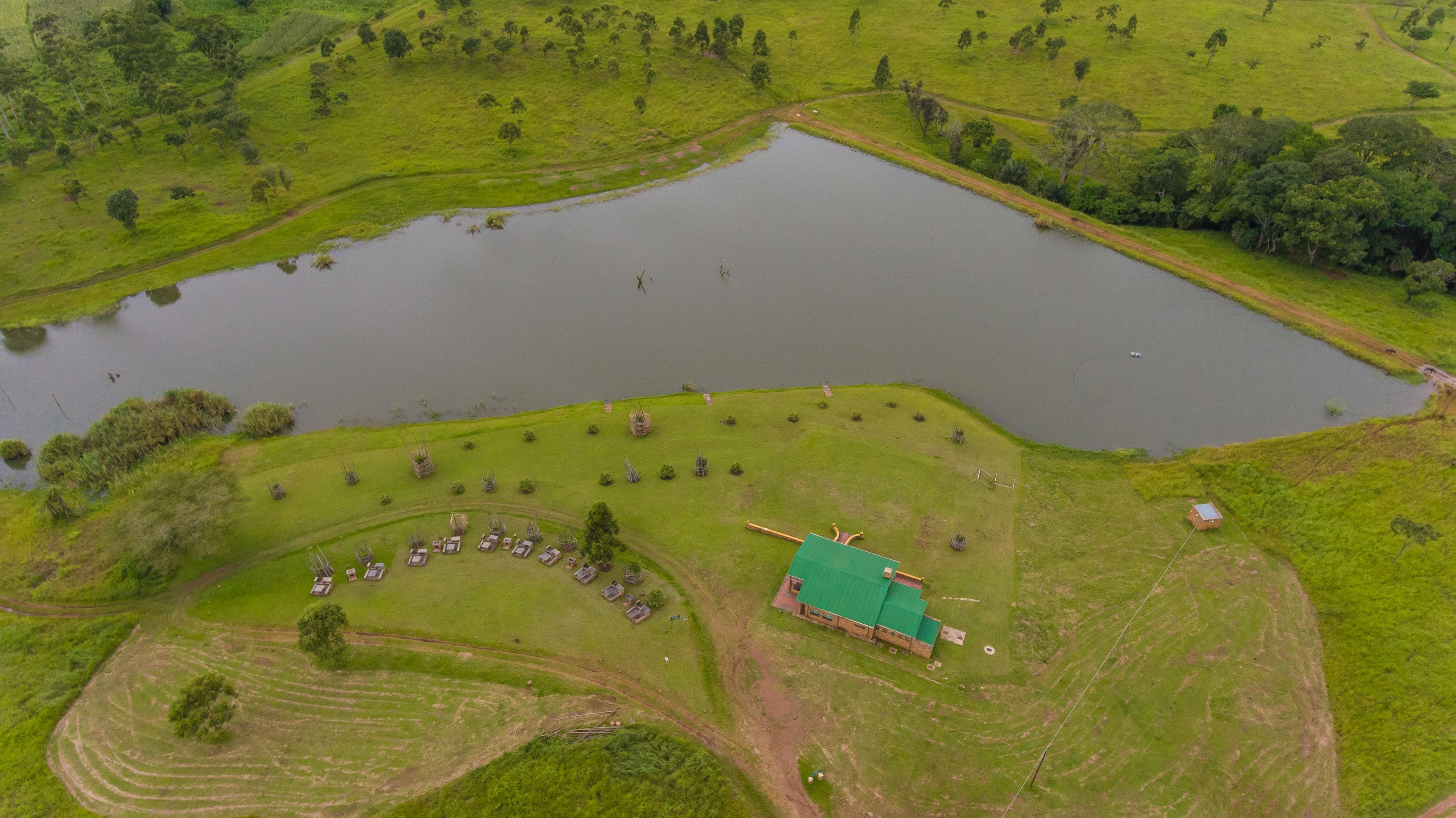 An aerial view of a property with a large pond, green fields, and a building with a green roof.