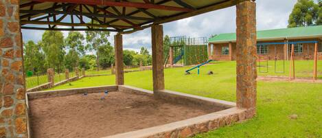 A covered outdoor area with stone pillars, a sandpit, and a playground in the background.