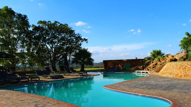A swimming pool with lounge chairs, a brick deck, and a view of trees and hills. - Game Haven Lodge (Chigumula)