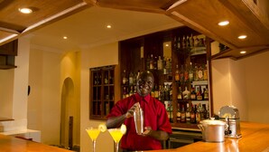 A bar area with a bartender, a bar counter, and a shelf of liquor bottles. - Game Haven Lodge (Chigumula)