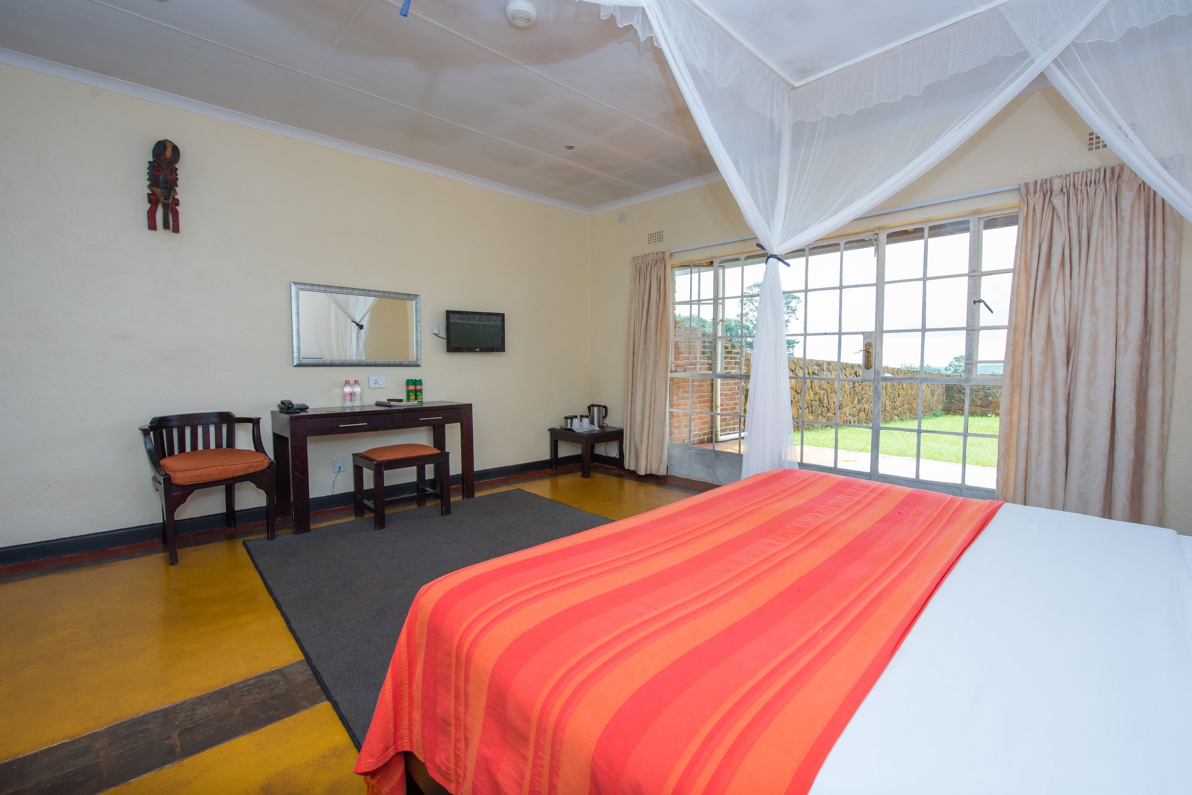 A hotel room with a bed, desk, chair, and a large window with curtains.