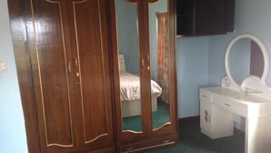 A bedroom with a wooden wardrobe, a white dresser with a mirror, and a bed with a blue wall.