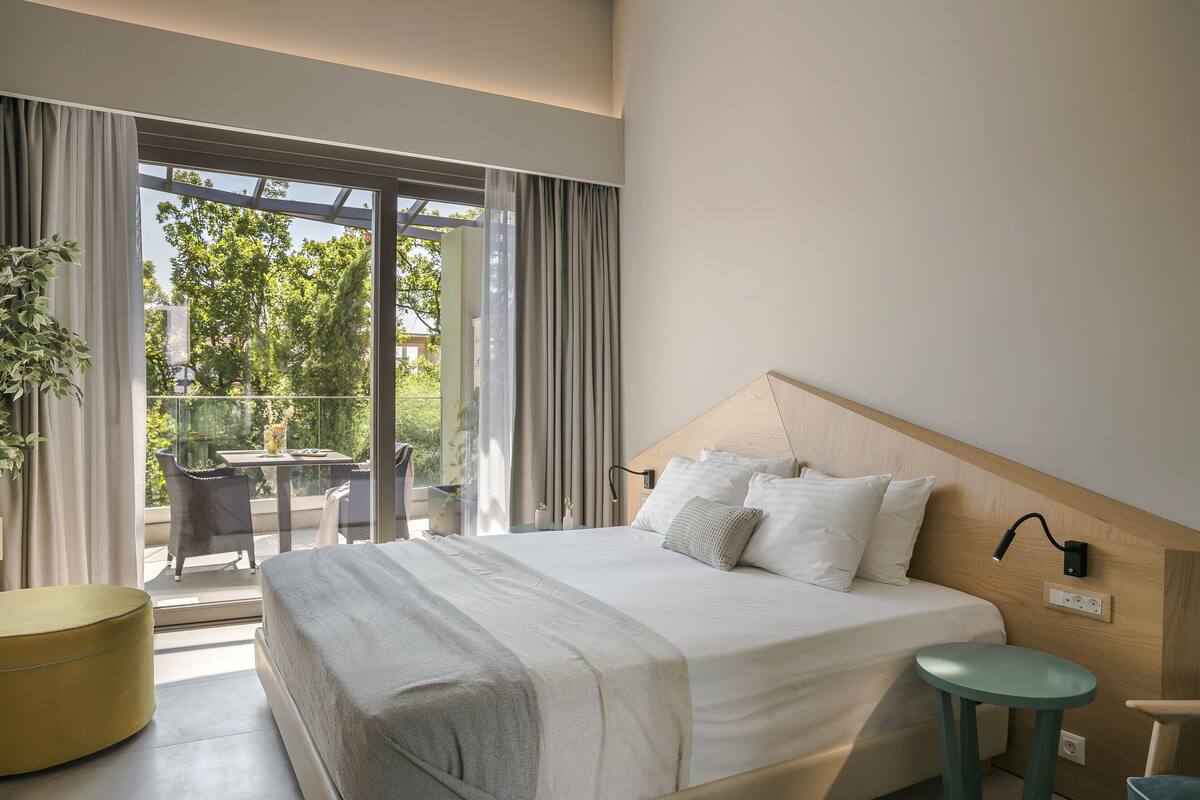 A modern hotel room with a large bed, a small round table, and a balcony with outdoor seating.