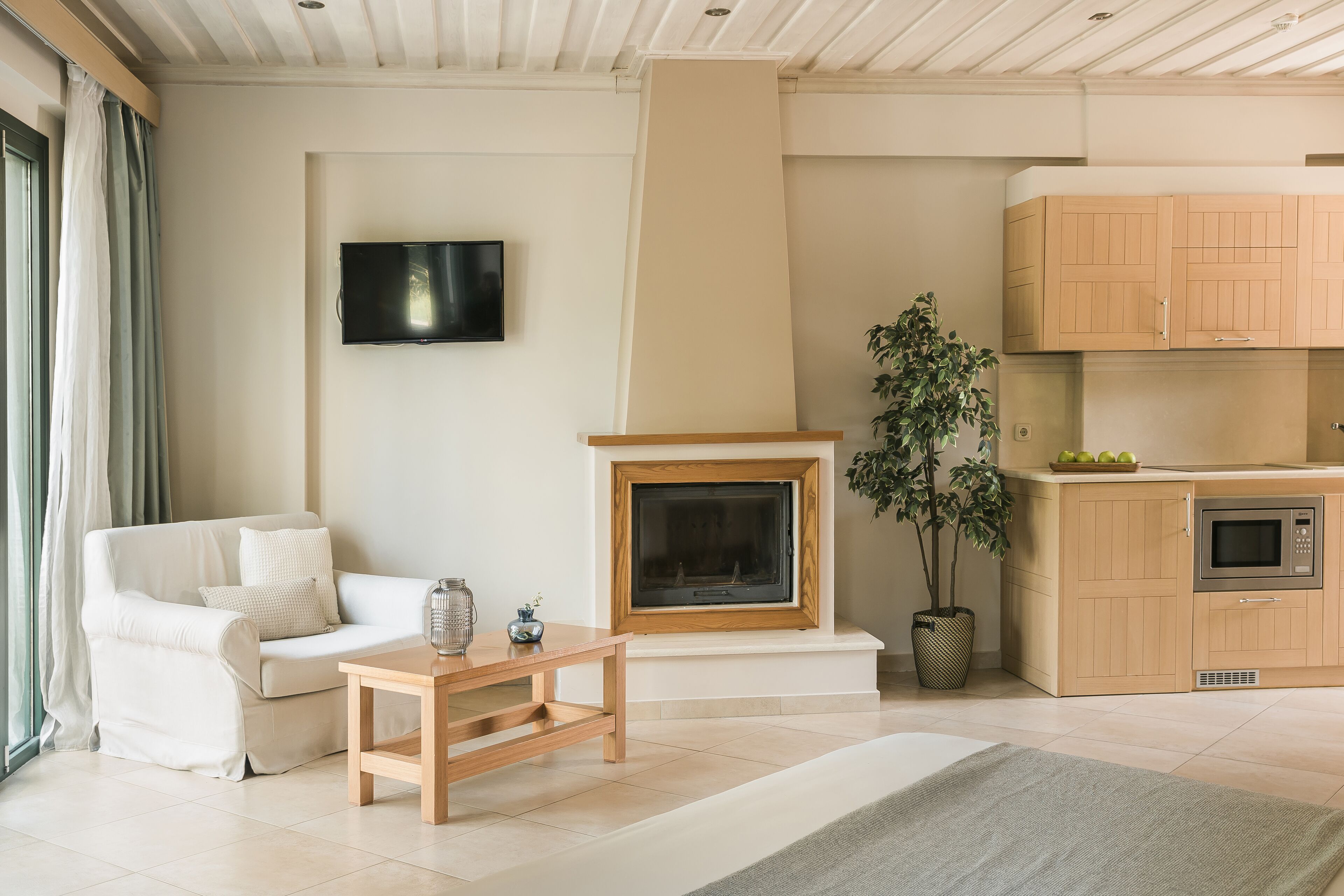 Un salon moderne doté d’une cheminée, d’un téléviseur à écran plat, d’un canapé, d’une table basse et d’un coin cuisine avec des meubles en bois et un four à micro-ondes.