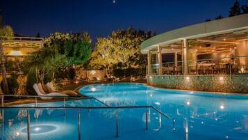 A swimming pool with lounge chairs, a restaurant area, and a stone wall.