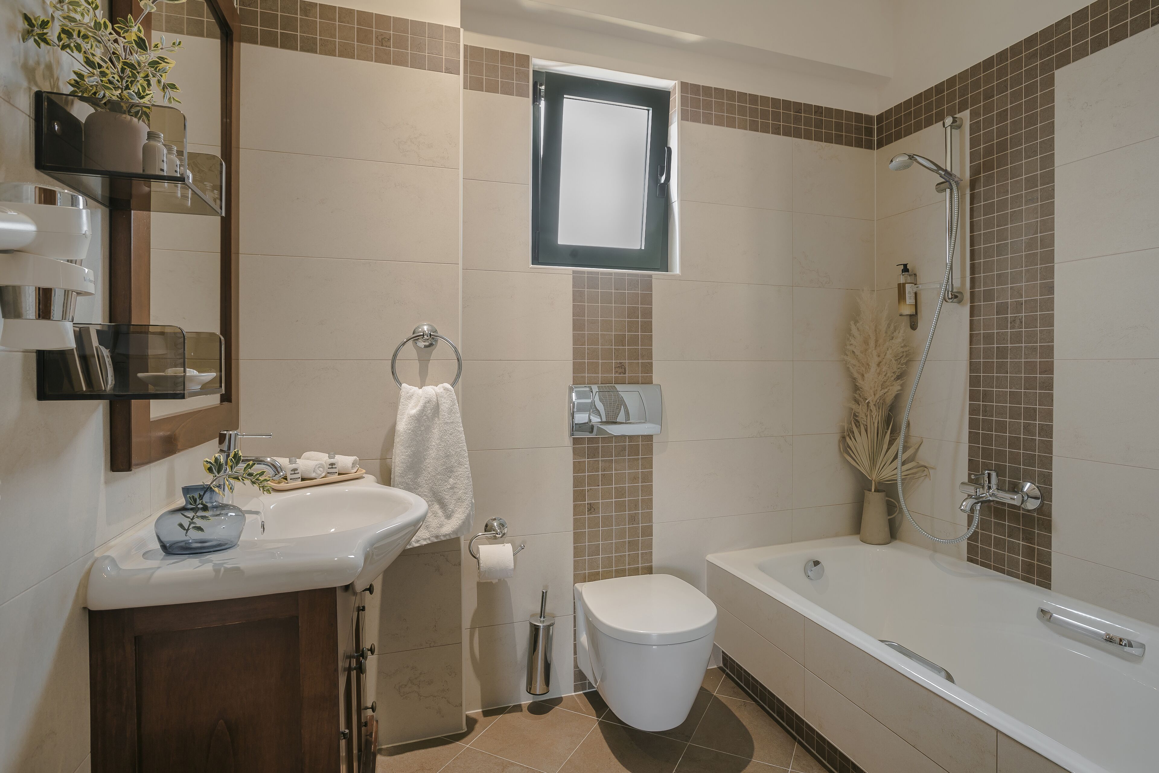 Un baño moderno con lavamanos, inodoro y bañera. Hay una ventana sobre el inodoro y un cabezal de ducha a la derecha.
