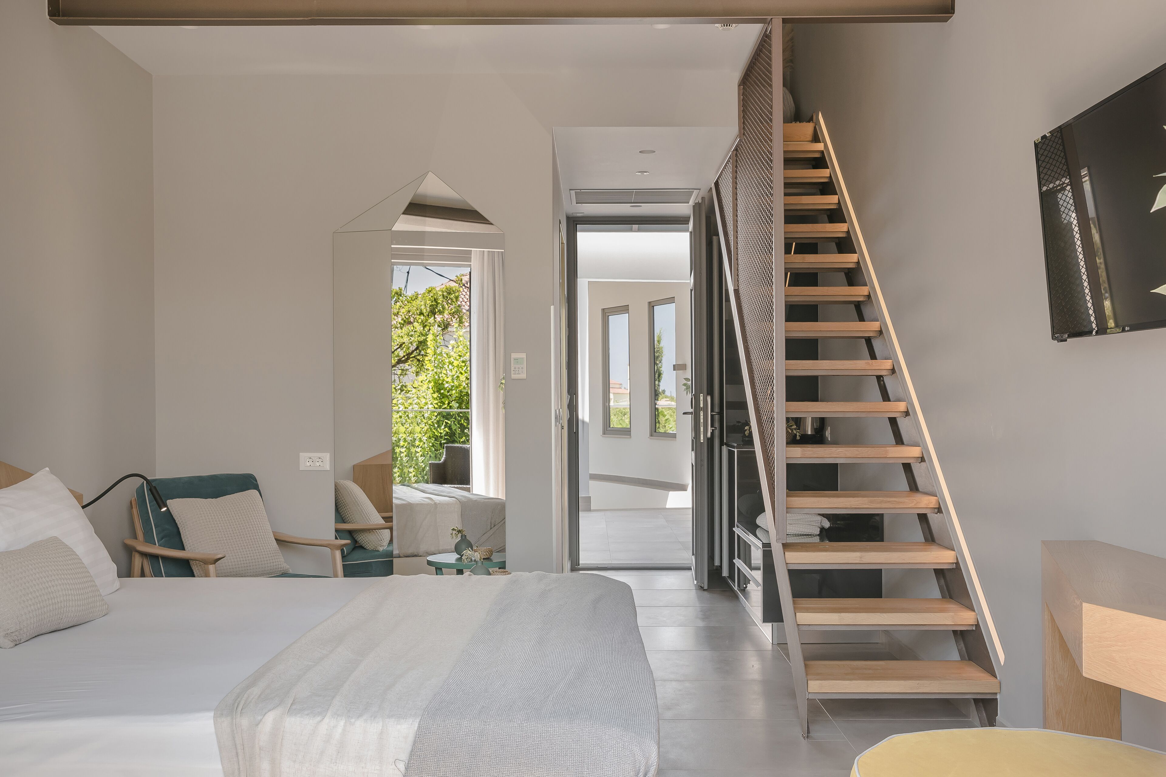 A modern bedroom with a large bed, a wooden staircase, and a view to an outdoor area.
