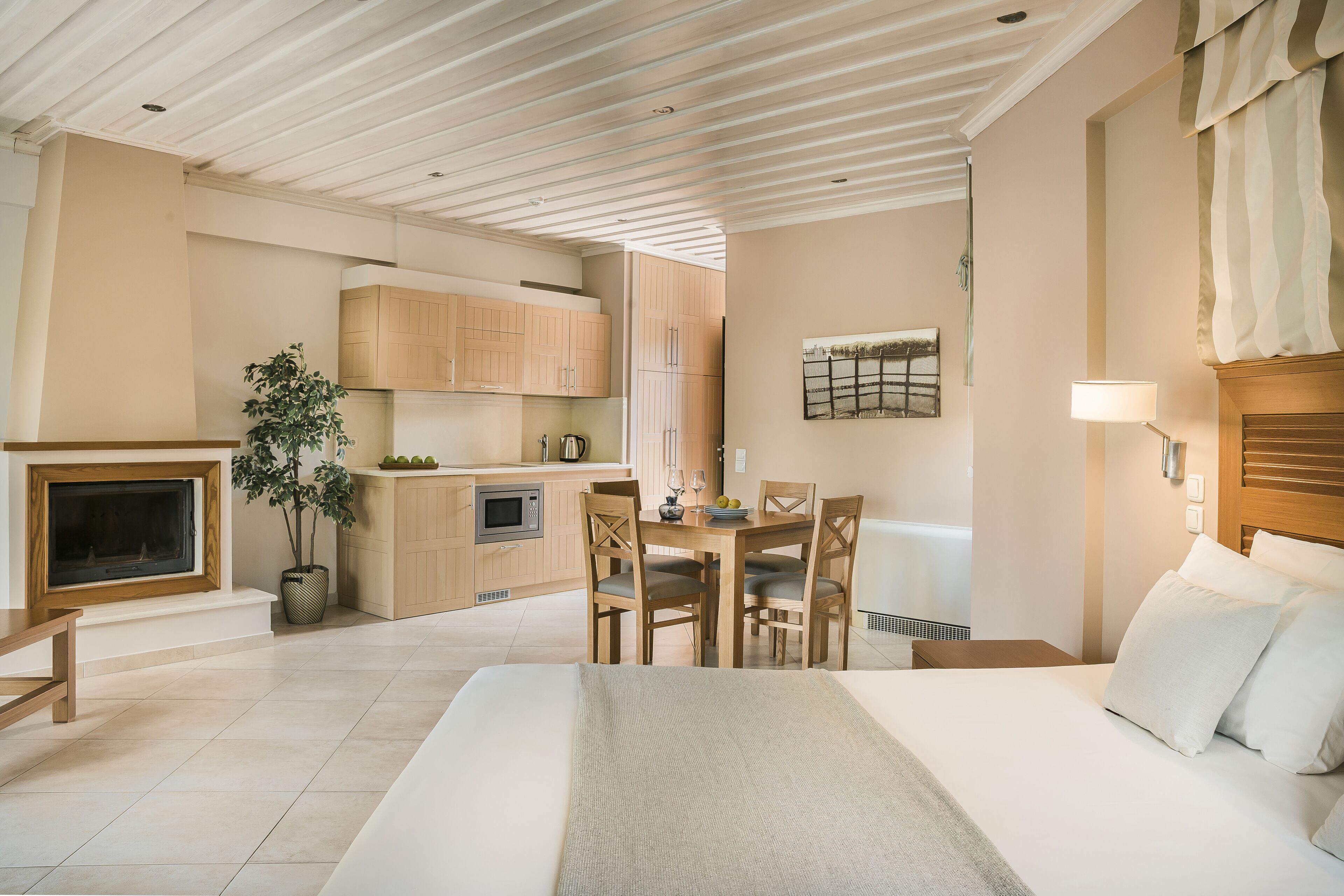 A modern hotel room with a large bed, a dining area, a kitchen, and a fireplace.