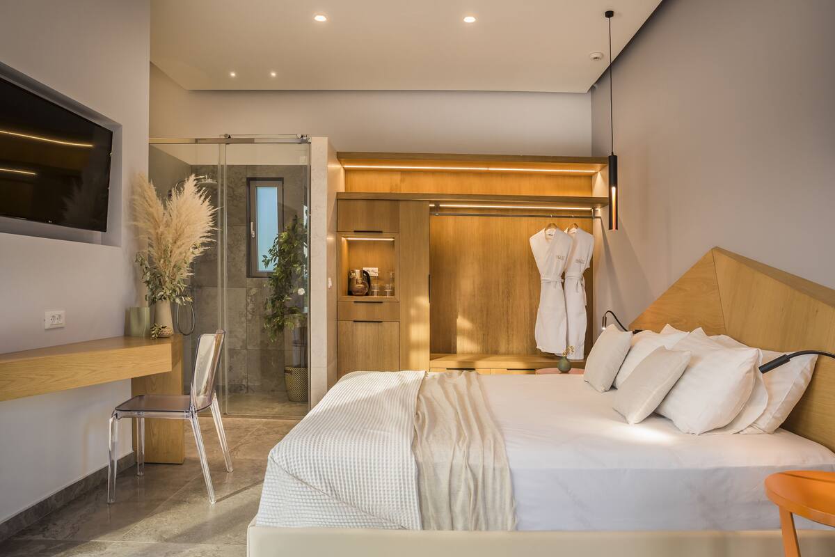 A modern bedroom with a large bed, a wooden headboard, a built-in TV, a glass shower enclosure, and a wooden wardrobe.