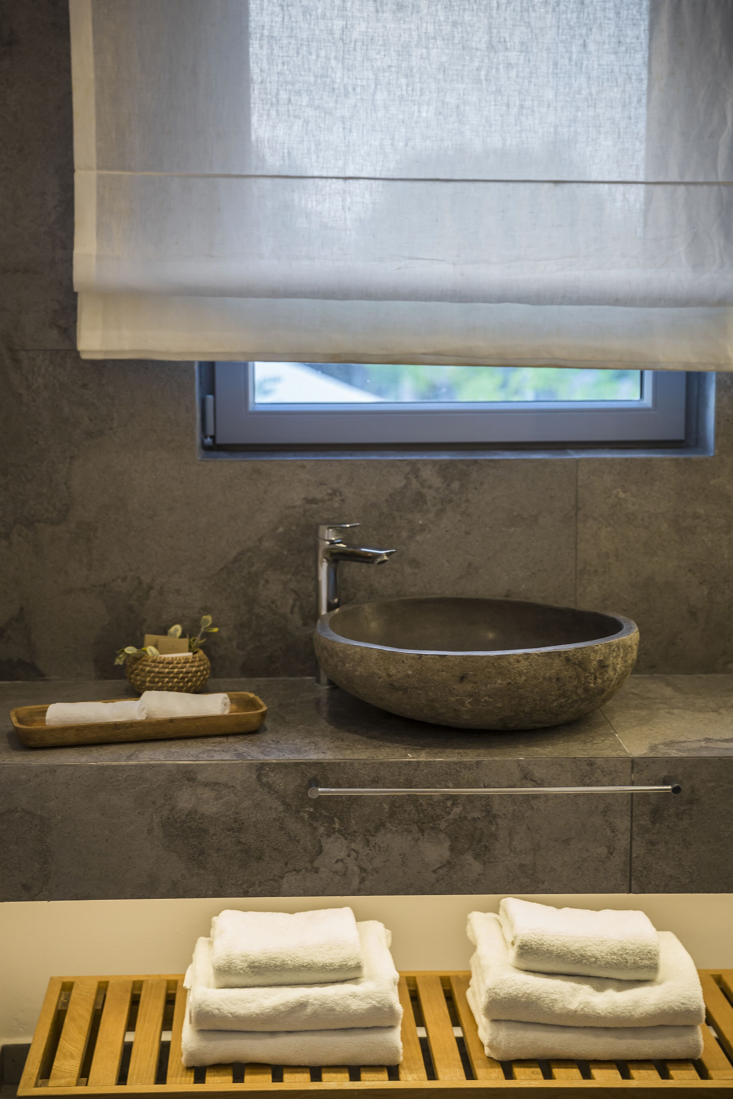 A bathroom with a stone sink, wooden towel rack, and a window with a view.