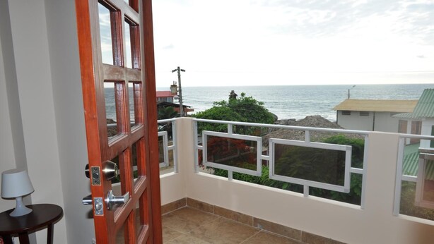 A balcony with a view of the sea, a wooden door, and a small table with a lamp. - Puerta Sol Inn (Manglaralto)