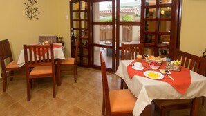 A dining area with a table set for breakfast, including plates, a basket of bread, and a bowl of fruit. - Puerta Sol Inn (Manglaralto)