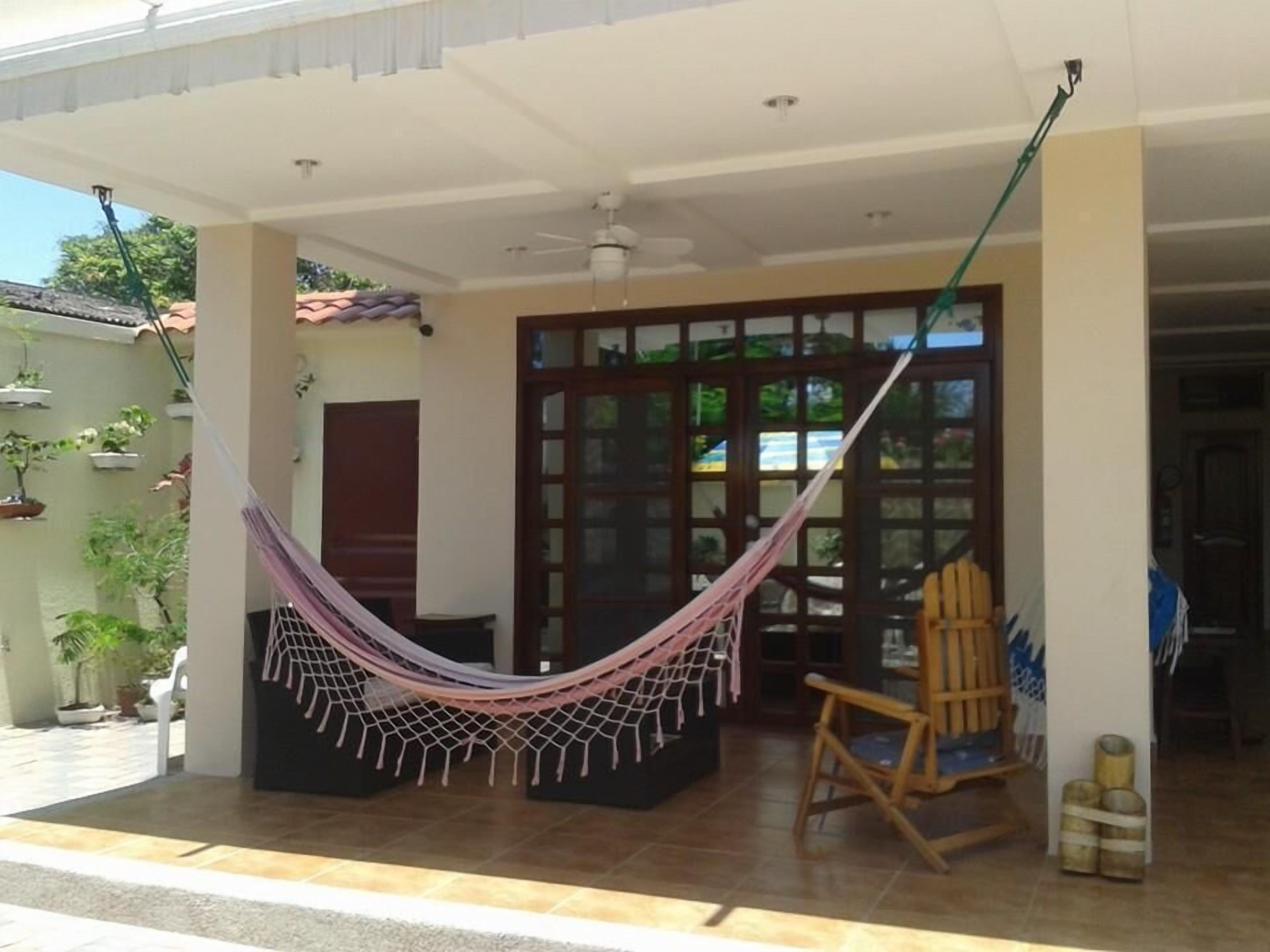 A covered porch with a hammock, a wooden chair, and a tiled floor.
