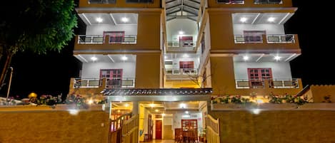 A multi-story hotel with a central entrance, balconies on each floor, and a well-lit facade.