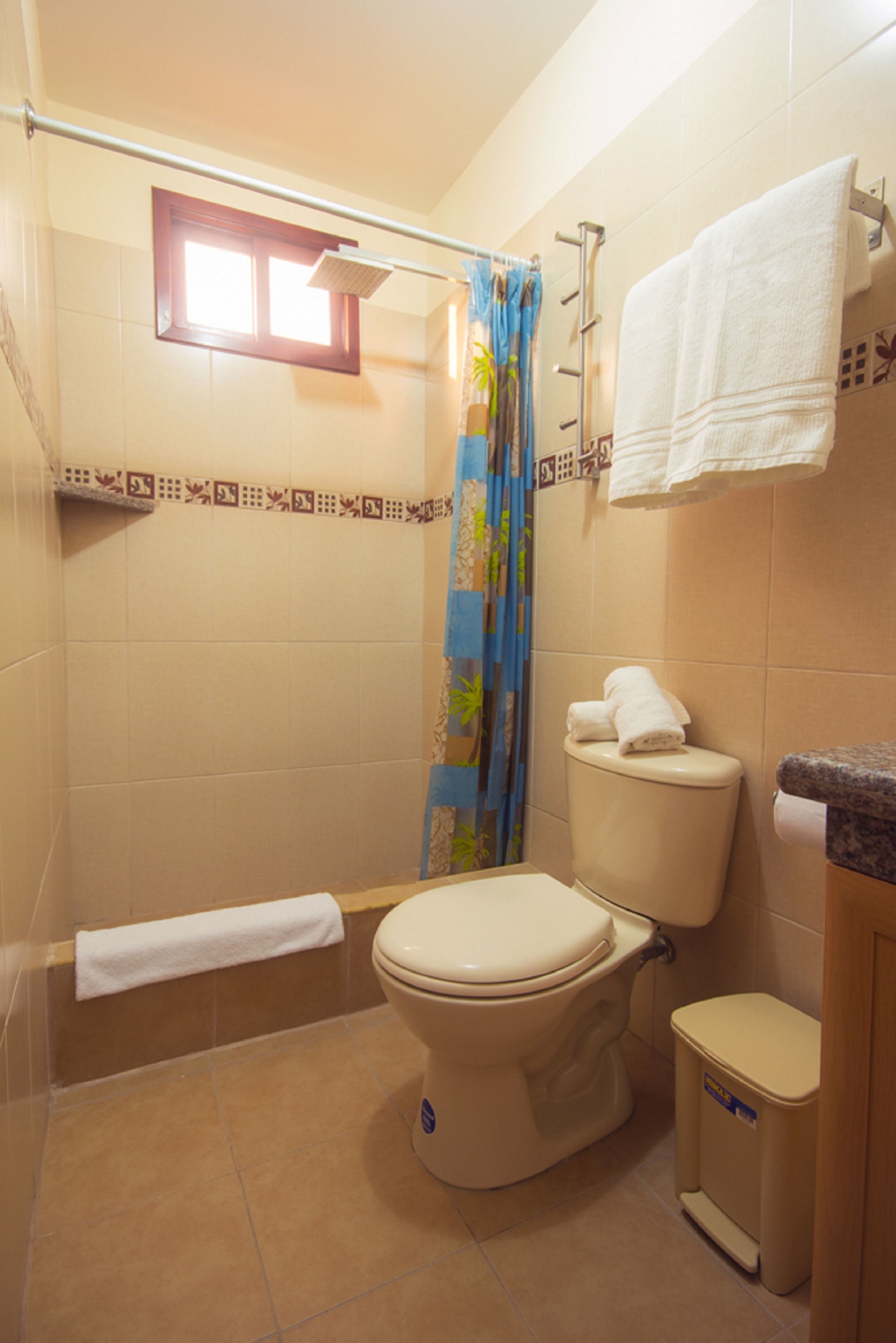 A bathroom with a toilet, a shower curtain, a towel rack, and a small window.