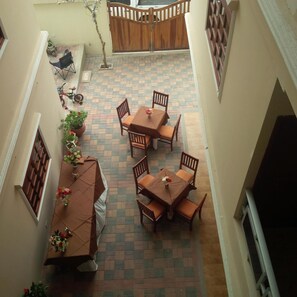 Un patio con zona de comedor, mesas y sillas, rodeado de muros y un portón de madera.