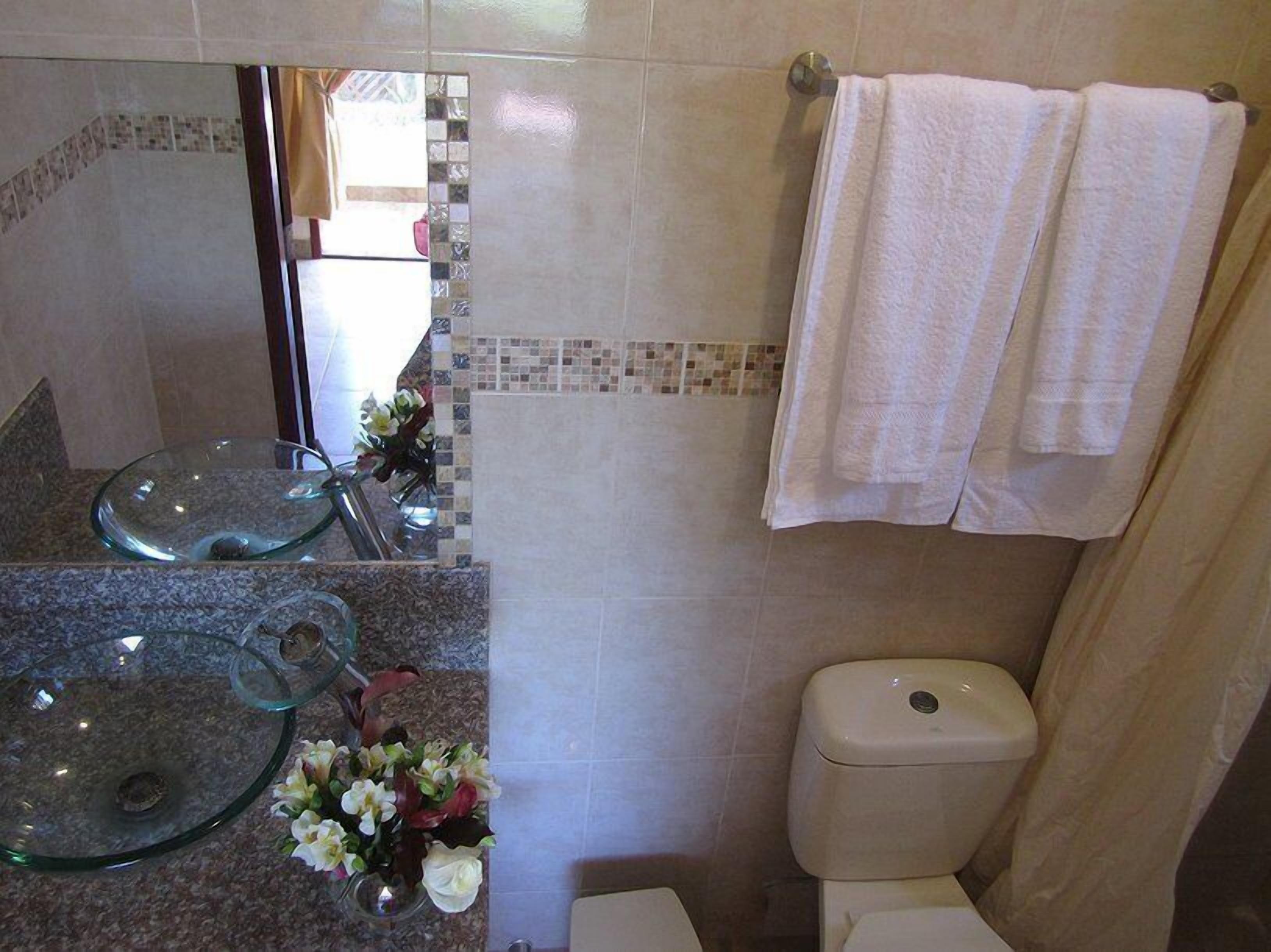 Un baño con un lavabo de vidrio, un inodoro y una cortina de ducha.