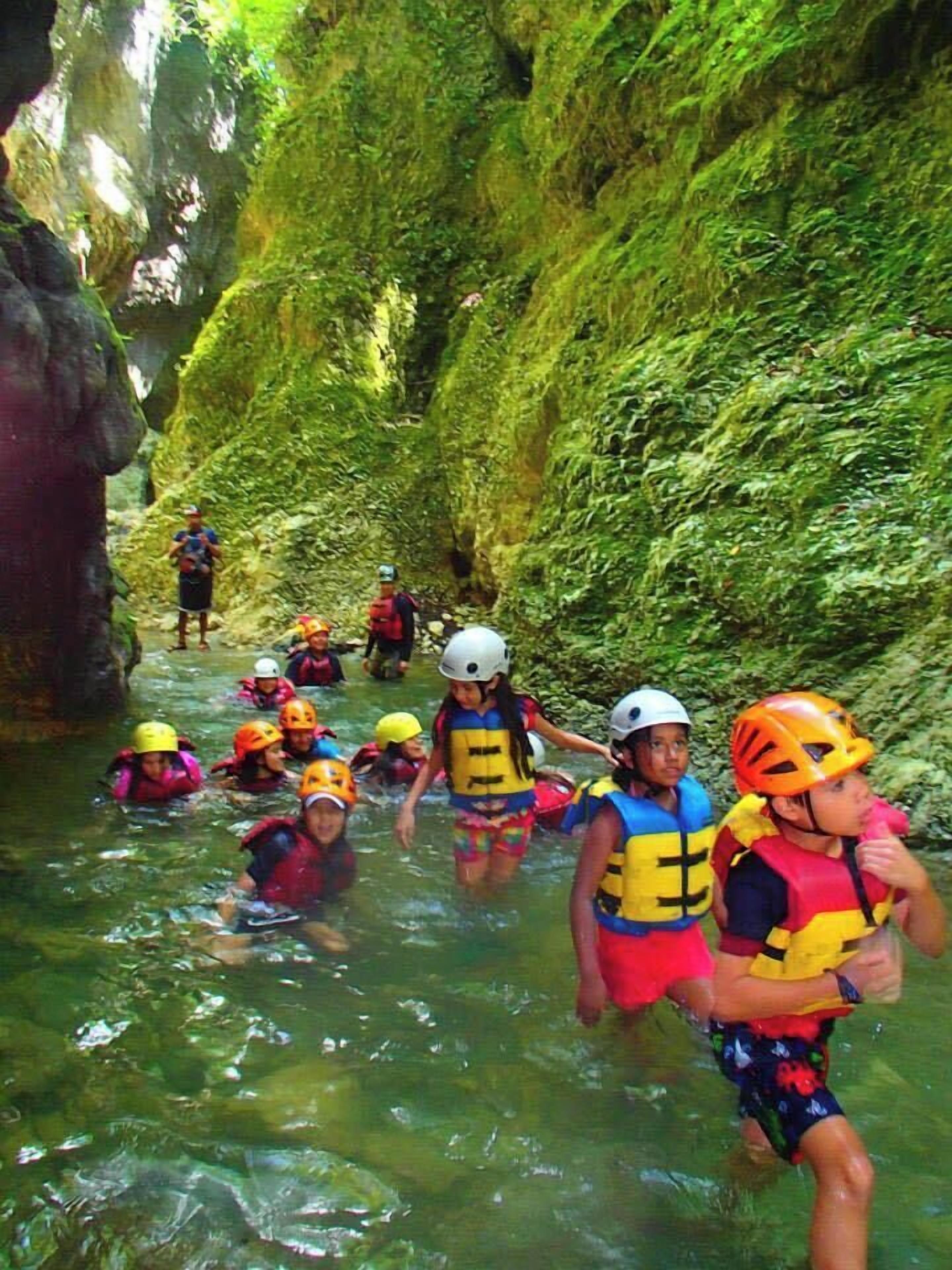 A group of people in a narrow, rocky waterway, wearing life jackets and helmets, suggesting a guided water activity.