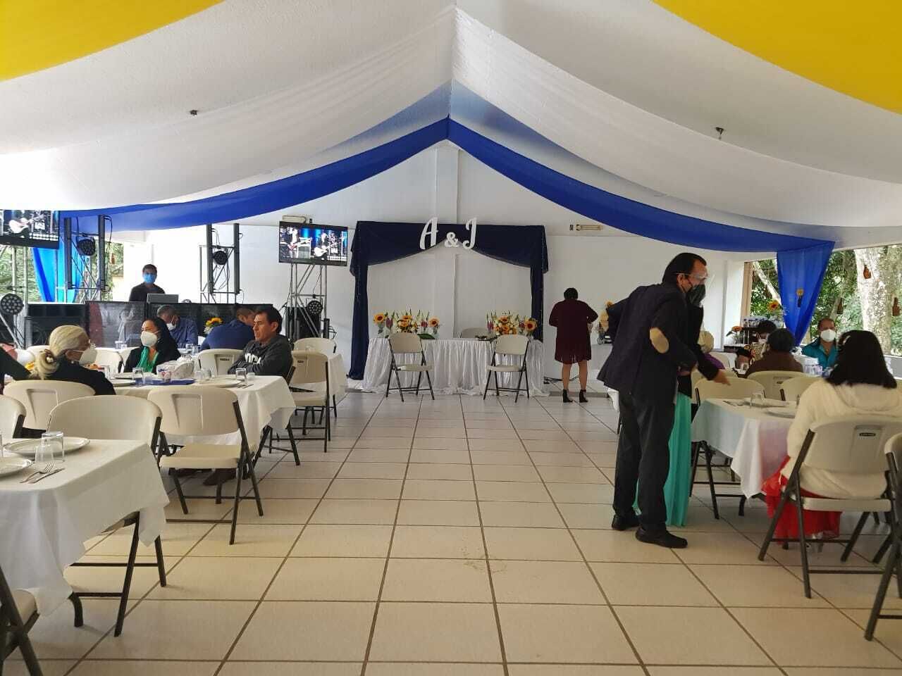 A banquet hall with white tables, blue drapes, and a stage area.