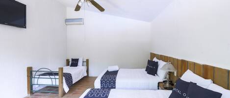 A hotel room with a large bed, two smaller beds, a ceiling fan, a TV, and a tiled floor.