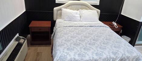 Quarto de hotel com cama, mesa de cabeceira, espelho, aquecedor e televisão presa à parede.