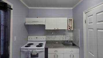 Una cocina compacta con armarios blancos, estufa, fregadero y microondas.