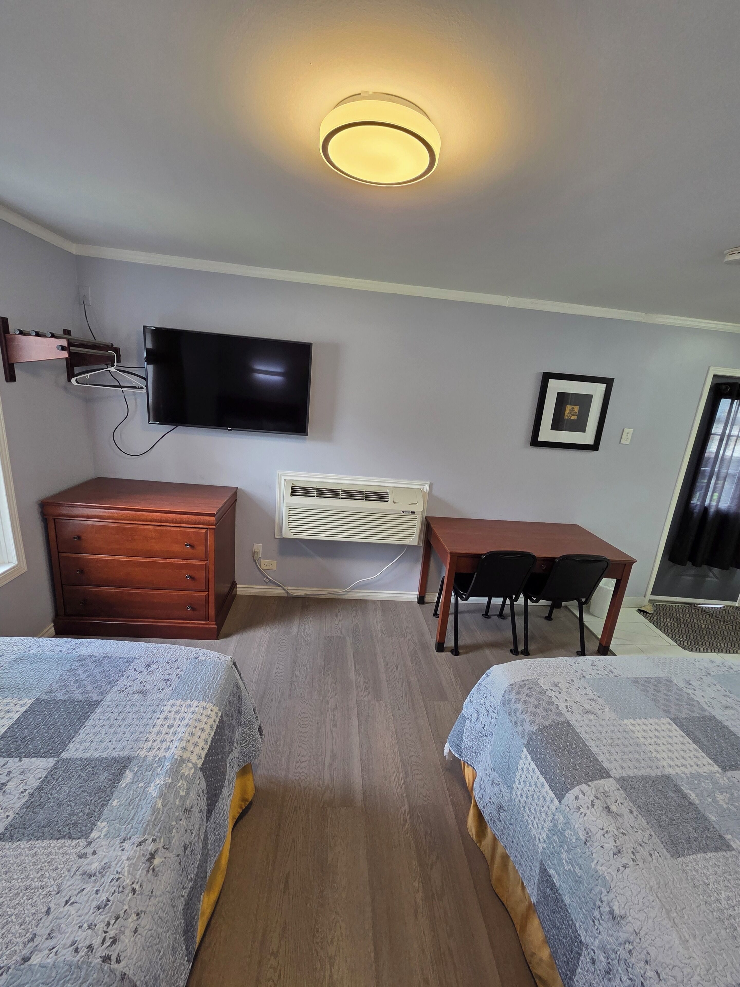 A room with two beds, a TV, a desk, and an air conditioning unit.