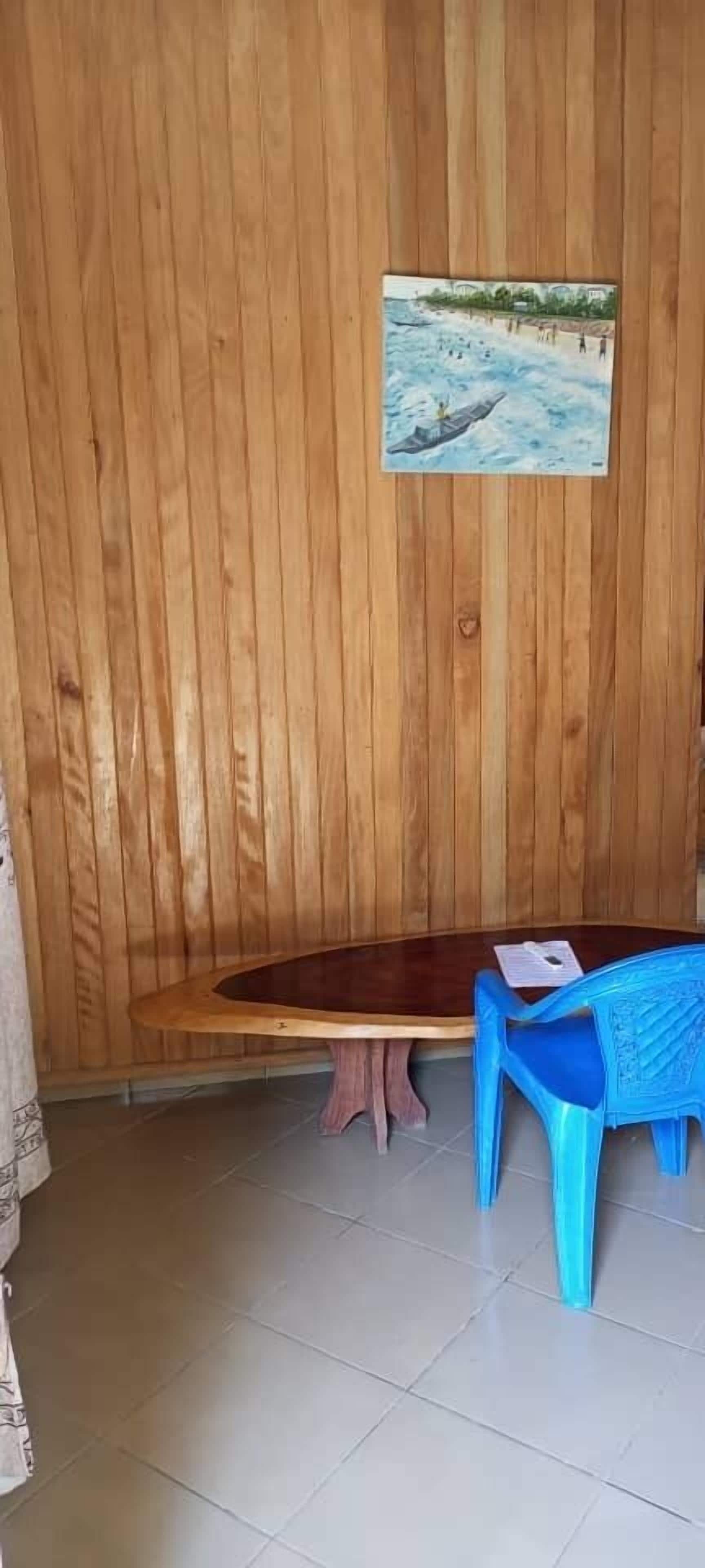 A wooden wall with a framed picture, a wooden bench, a small table, and a blue plastic chair.