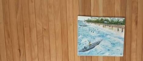 A wooden wall with a framed picture, a wooden bench, a small table, and a blue plastic chair.