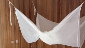 Una cama de madera con dosel blanco, una mesita de noche de madera y un tapete azul y beige sobre suelo de baldosas.