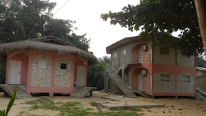 Un edificio de dos pisos con fachada de piedra y una estructura con techo de paja adyacente.