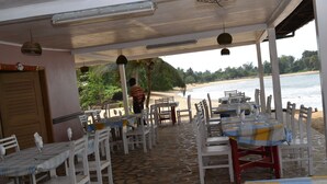 Un espacio de comedor al aire libre con mesas y sillas, vista a la playa y una puerta de madera.