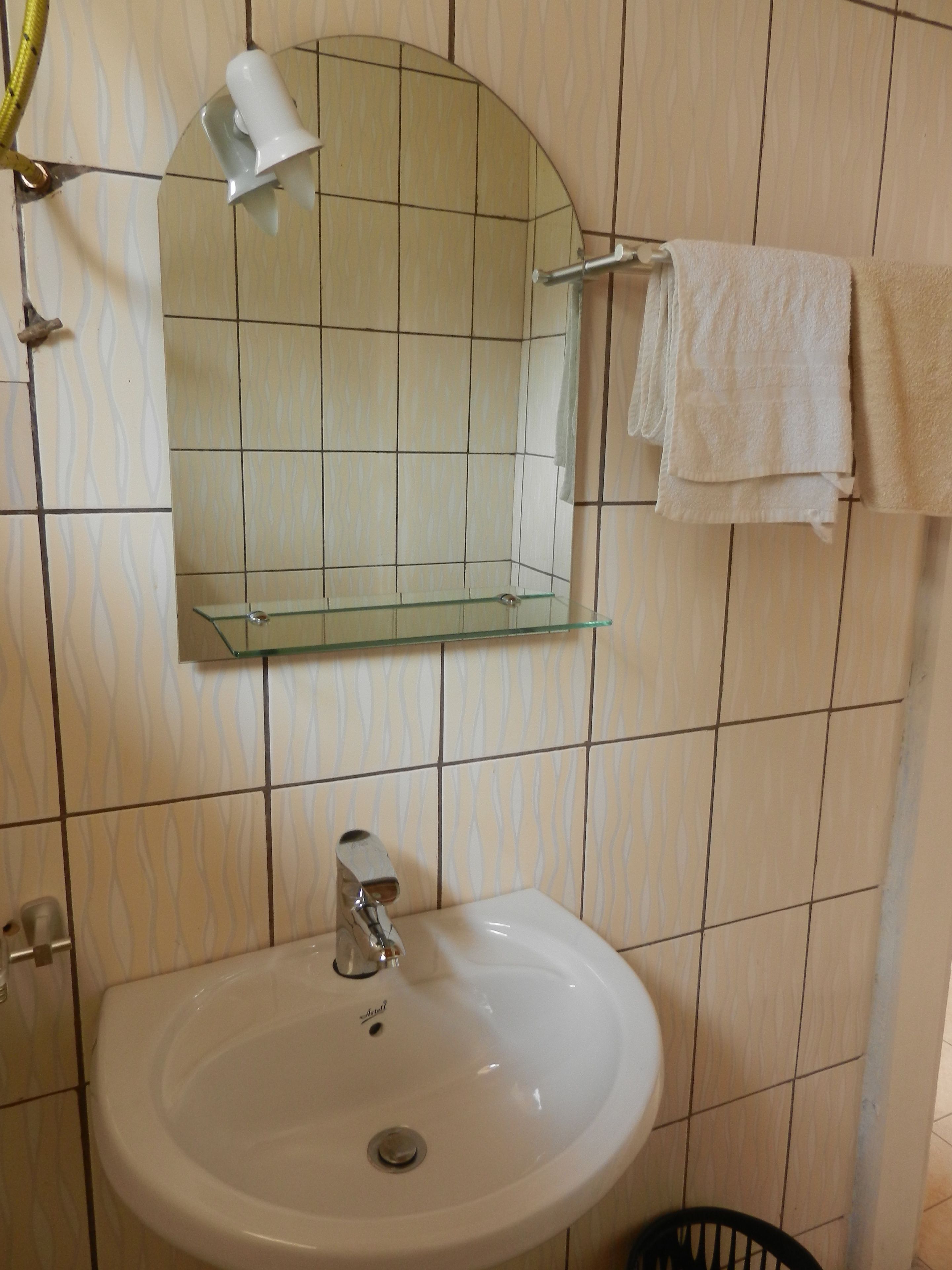 Ein Badezimmer mit einem weißen Waschbecken, einer Glasablage darüber, einem Spiegel und einem Handtuchhalter mit einem Handtuch.
