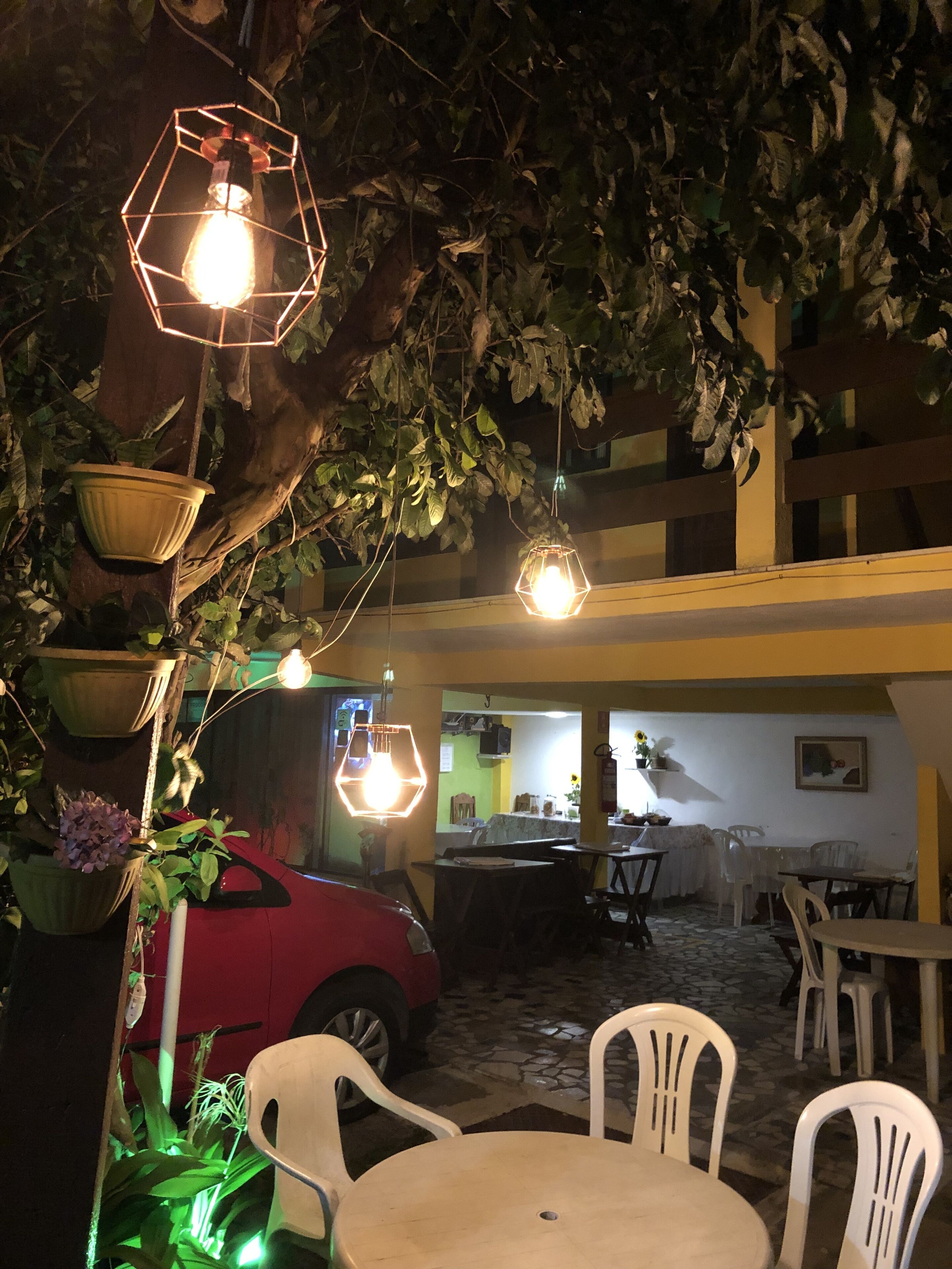 Un espacio al aire libre con mesas, sillas, luces colgantes y plantas en macetas.